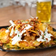 black plate with potato chips, cheese, sour cream and a beer