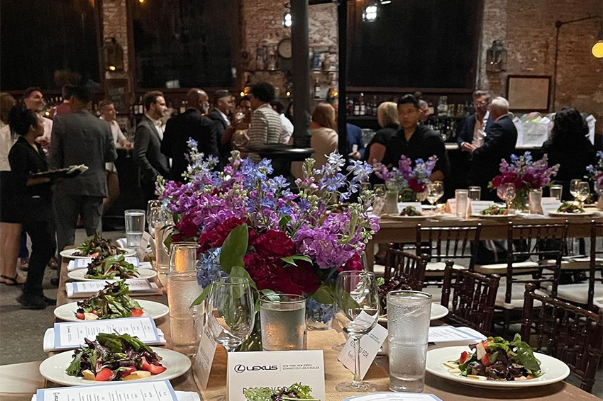 View of a table with purple flowers in the middle and plates with people in the background at our corporate holiday event venue near SoHo.