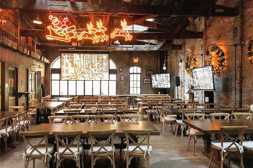 View of the interior of our company party venue near SoHo, NYC, with numerous empty tables and stools and a Santa Claus with sleigh decoration overhead.