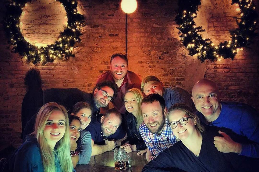 Group of men and women smiling at the camera with Christmas wreaths in the background at our holiday party venue near SoHo, New York City.